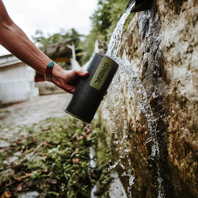 Befüllen einer tragbaren Wasserflasche aus einem Steinbrunnen mit einem Grayl Geopress Wasserfilter für sicheres Trinkwasser.