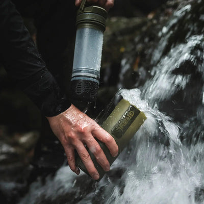 Eine Person füllt einen Grayl® Ultrapress Wasserfilter 500ml für effektive Wasserreinigung aus einem Bergbach.