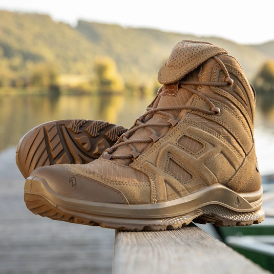 Ein Paar braune HAIX® BLACK EAGLE® ATHLETIC 2.0 V GTX Wanderstiefel auf einer Holzoberfläche mit natürlicher Wasserkulisse.