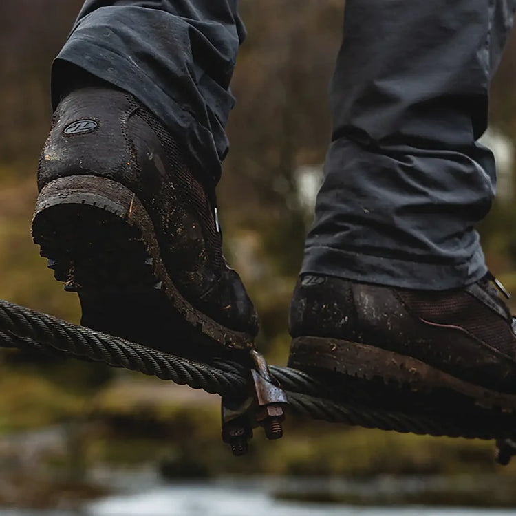 Nahaufnahme der schlammigen Stiefel einer Person, die über eine Hängebrücke läuft.