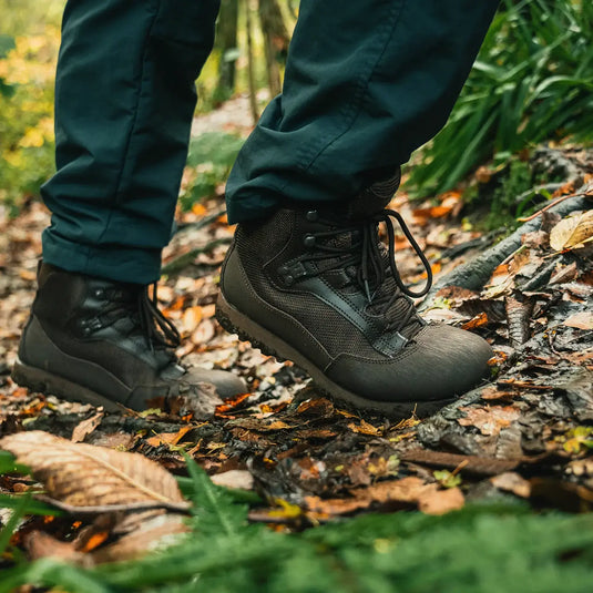 Eine Person mit HIGHLANDER® „Pentland“ Stiefel wandert durch einen Wald mit abgefallenen Blättern.