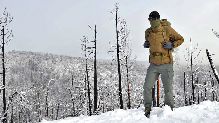 Wanderer mit Rucksack und Trekkingstöcken steht in einem verschneiten Wald mit kahlen Bäumen.