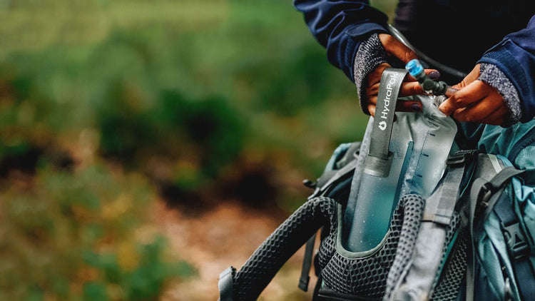 Eine Person befestigt im Freien eine Wasserflasche an der Seitentasche eines Rucksacks.