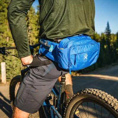 Radfahrer mit einem Hydro Flask® 5 L Down Shift™ Hydration Hip Pack und einer blauen Satteltasche montiert auf einem Mountainbike im Freien.