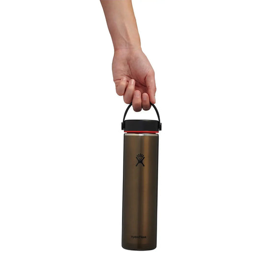 Eine Hand hält eine Hydro Flask® 24 oz (710 ml) Lightweight Wide Mouth Trail Series™ isolierte Wasserflasche mit schwarzem Verschluss und Tragegriff.