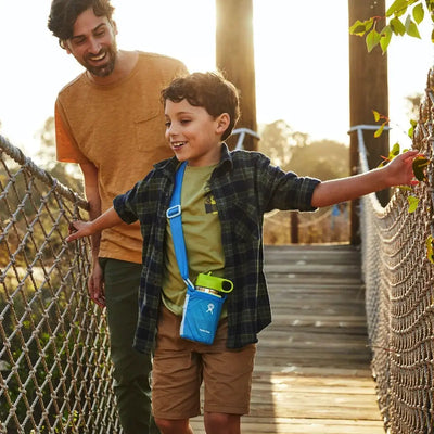 Vater und Sohn genießen mit einer Hydro Flask® 12 oz (355 ml) Kids Wide Mouth einen Spaziergang auf einer Hängebrücke im Freien.