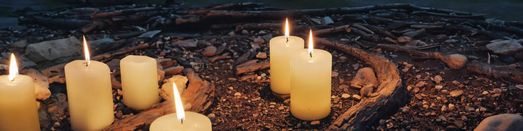 Fünf brennende Kerzen auf einer felsigen Oberfläche in der Nähe von Holzstücken in der Abenddämmerung.