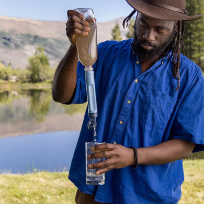 Mann filtert Trinkwasser im Freien mit einem Strohhalm der LifeStraw® Peak-Serie in ein Glas.