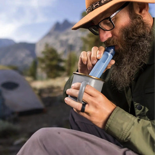 Mann mit Bart nippt beim Camping in den Bergen an Trinkwasser aus einem Strohwasserfilter der LifeStraw® Peak-Serie.