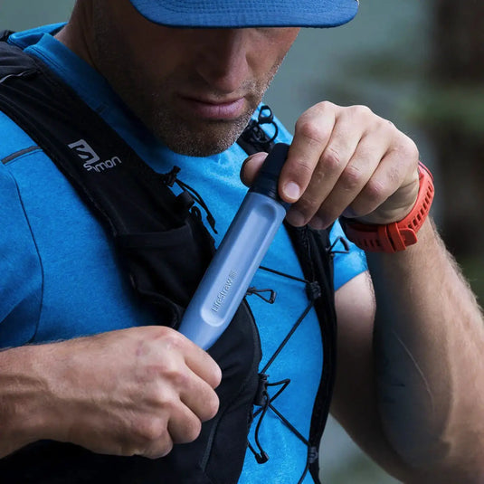Mann überprüft einen tragbaren LifeStraw® Peak Series Straw-Wasserfilter, während er einen Trinkrucksack trägt.