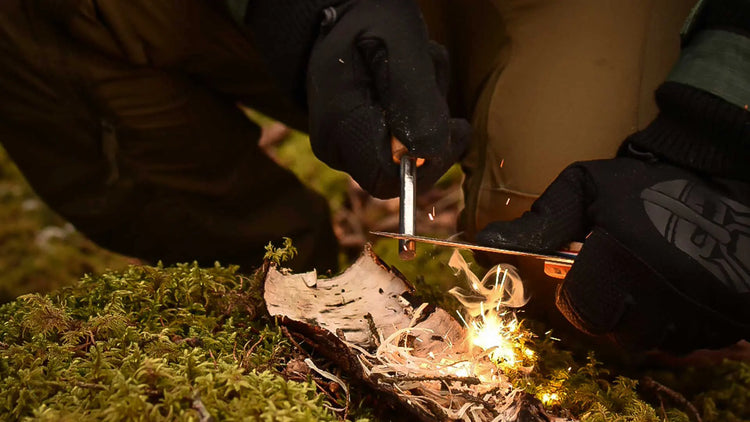 Anzünden eines Feuers mit einem Eisenstab auf einem Stück Birkenrinde im Freien.