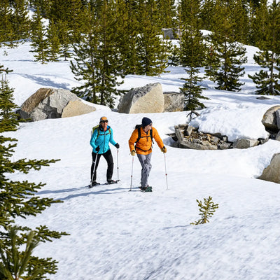 Zwei Wanderer mit Trekkingstöcken und MSR® Revo™ Trail - Schneeschuhen auf einem verschneiten Bergweg.