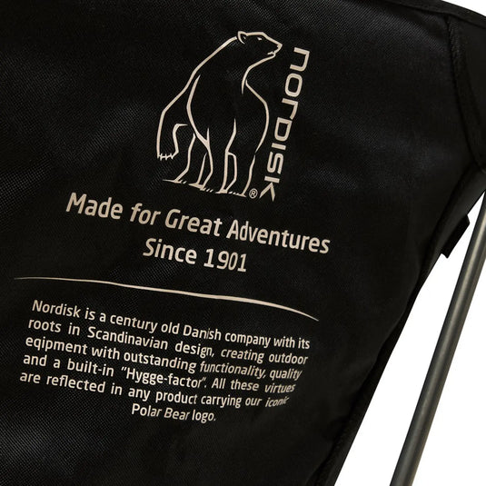 Nahaufnahme eines Nordisk® Marielund Campingstuhl-Etiketts, das das Erbe und die Qualitäten der Marke hervorhebt, mit dem ikonischen Eisbärenlogo auf einem leichten Campingstuhl.