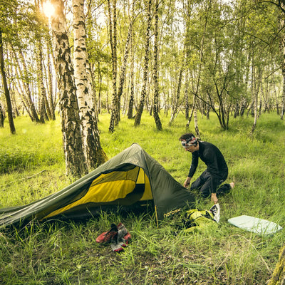 Eine Person baut in einem Birkenwald ein Nordisk® Lofoten 1 ULW Zelt auf.