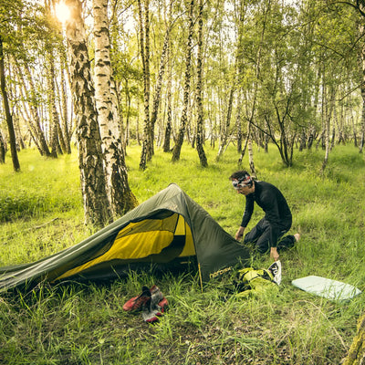 Ein Camper baut in einem Birkenwald ein ultraleichtes Nordisk® Lofoten 2 ULW Zelt auf.