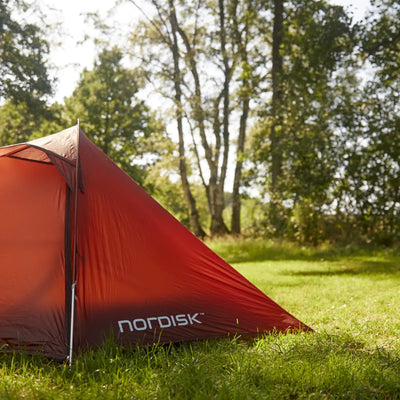 Rotes Campingzelt Nordisk® Lofoten 2 ULW Zelt auf einer Wiese mit Bäumen im Hintergrund.