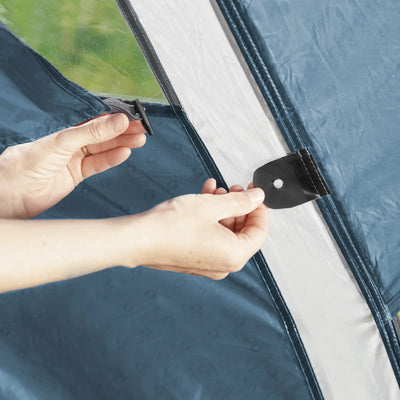 Person, die ein Outwell® 5-Personen Zelt - Earth 5-Zelt mit einem schwarzen Spanngurt auf einem Outwell-Campingplatz sichert.