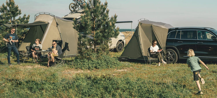 Familie genießt einen Campingausflug in der Nähe ihres Autos und ihrer Zelte auf einer Wiese.