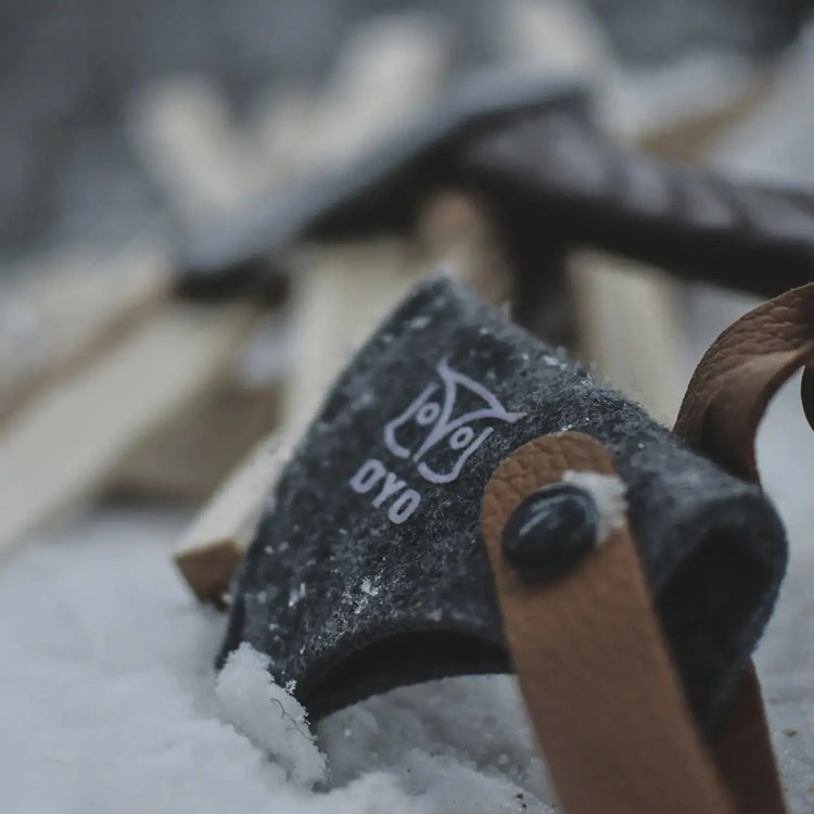 Eine ØYO Vikinger Axt mit Stahlklinge mit Ledergriffbezug ruht auf verschneitem Boden neben gehacktem Holz.