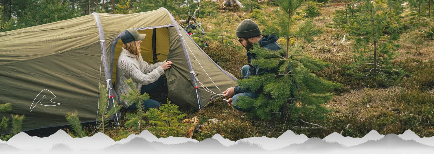 Zwei Personen bauen auf einer Waldlichtung ein Zelt auf.