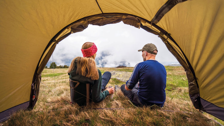 Zwei Personen sitzen am Zelteingang und genießen den Blick auf die Berge.