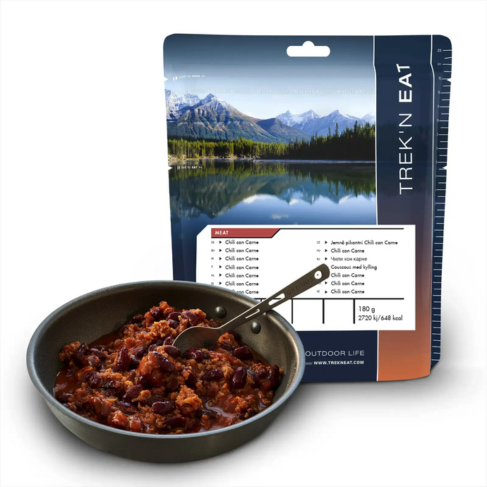 Trek'n Eat Chili con Carne-Mahlzeit für Outdoor-Abenteuer mit einer malerischen Bergkulisse auf dem Etikett, angezeigt neben einer zubereiteten Portion in einer Pfanne.