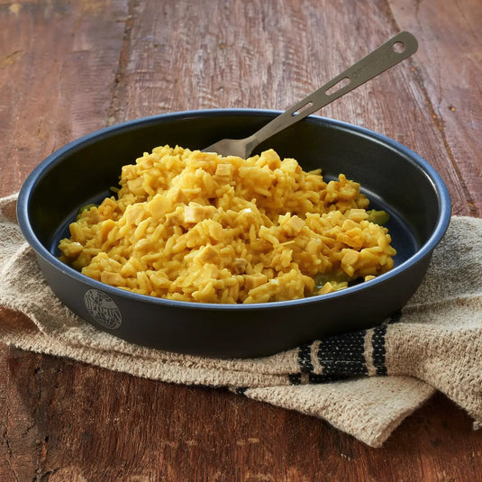 Rührei in einer beschichteten Bratpfanne mit Trek'n Eat Huhn in Curryreis auf einer Holzunterlage.