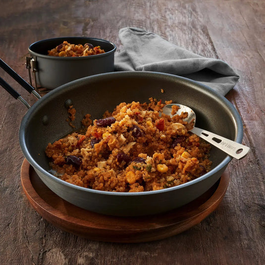 Eine Pfanne gekochtes Trek'n Eat Quinoa Mexikanische Art vegan mit gemischten Zutaten auf einem Holztisch.